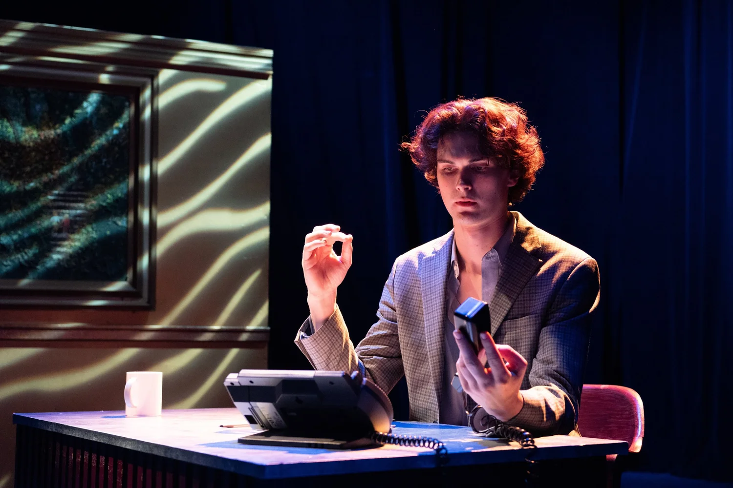 A photo of an actor sitting at a desk holding a telephone.